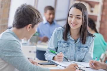 Un étudiant et une étudiante travaillent ensemble à une table, échangeant autour de leurs notes, dans une salle d’étude.