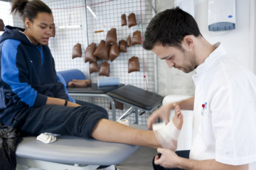 Un professionnel de santé bande la cheville d’une personne en consultation.